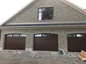 Walnut oak Clopay Gallery 12-foot door with elegant long panels and arch vertical grille windows
