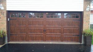 Walnut oak Clopay Coachman door with elegant long panels and arch-3 grille windows