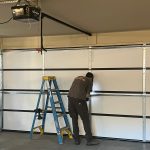 Garage door technician installing a new white garage door with a Raynor opener.