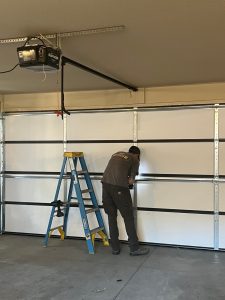 Garage door technician installing a new white garage door with a Raynor opener.