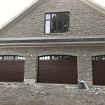 Three dark wood garage doors installed on a stone house exterior.