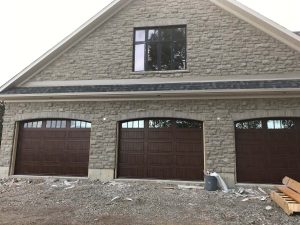 Three dark wood garage doors installed on a stone house exterior.