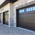 Two dark wood-style garage doors installed on a stone exterior home with decorative window panels.