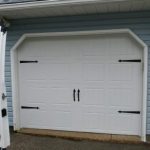 Newly installed white residential garage door with service van parked nearby